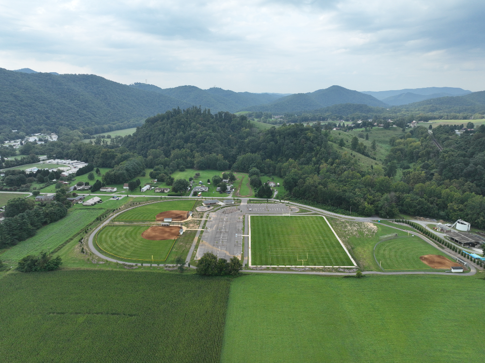 An aerial view of Creed Fields Park showing the layout of the entire facility with a walking track around the perimeter with a view of the surrounding mountains on a cloudy summer day.
