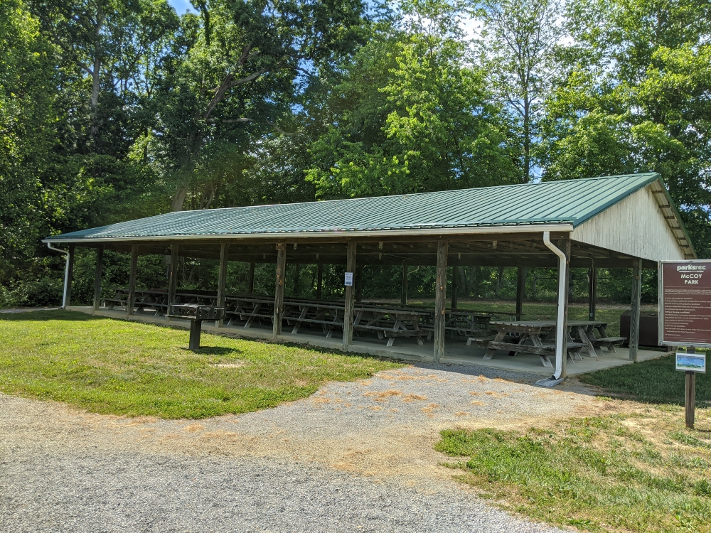 The picnic shelter at McCoy Park has a row of trees in the back and a gravel ADA accessible path in the front.