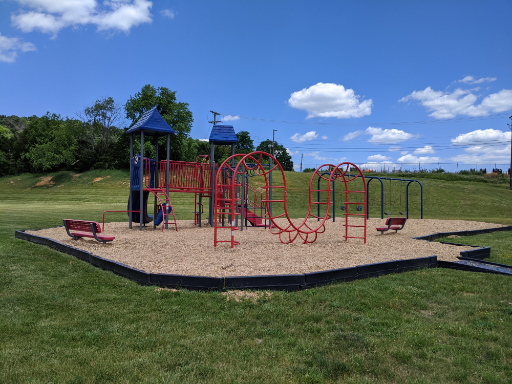 The playground at Motor Mile Park features slides, climbing areas, and a swing set with a mulch base in an open green space.