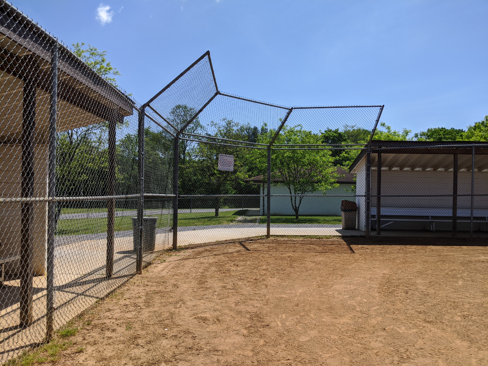 A view of the youth baseball field dugouts and backstop on a sunny summer day.