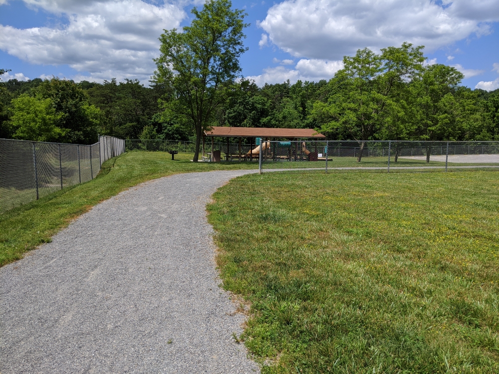 The gravel walking track at Plum Creek Park curves around the baseball field past the picnic shelter on a sunny summer day.