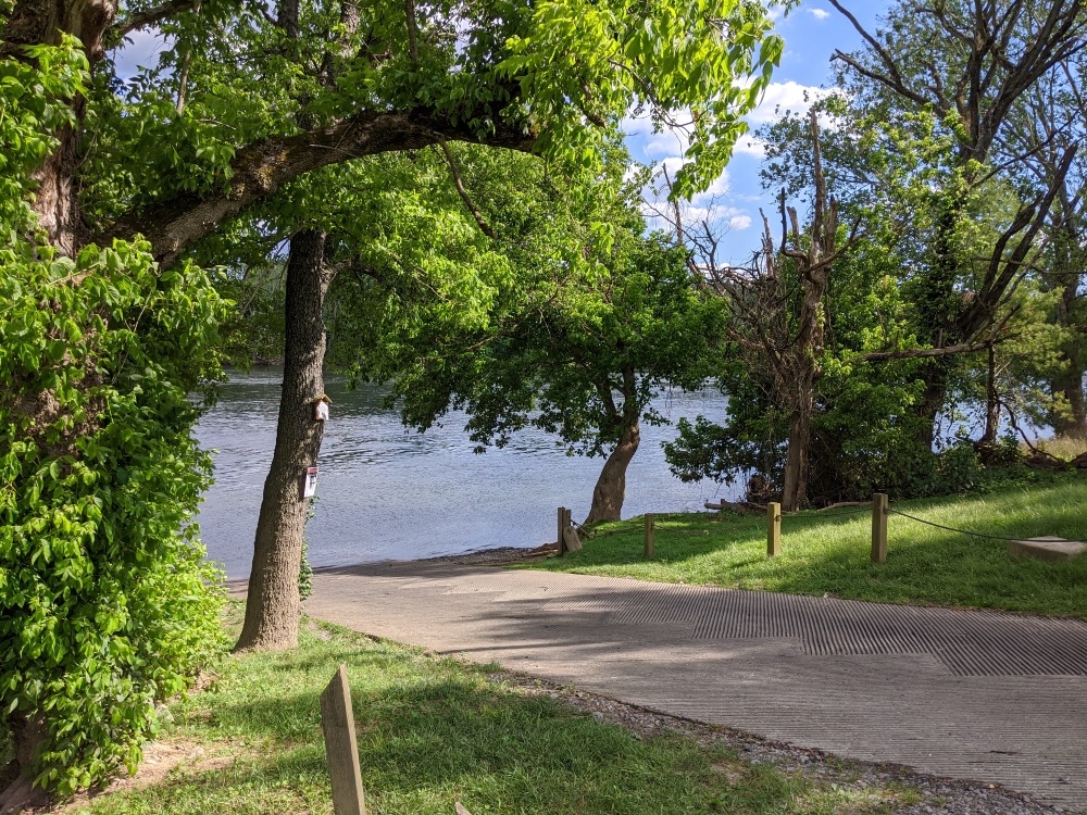 The Whitethorne Boat Launch is shown leading down to the New River and is flanked by trees and grassy areas in the late afternoon sun on a summer day.