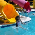 A child goes down the big slide and makes a splash at the Frog Pond Pool on a sunny summer day.