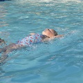 A swim instructor coaches a young swimmer in the backstroke.