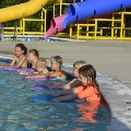A small group of children listen to their swim instructor teach water skills.