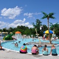 Guests dip their toes into the water while children play at the Frog Pond Swimming Pool on a sunny summer day.